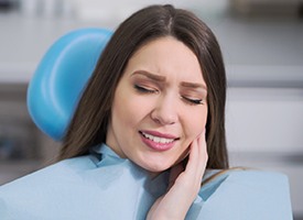 Woman in dental chair holding face